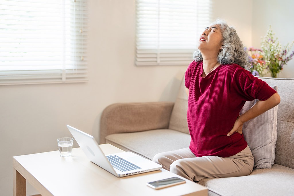 Older lady holding her lower back in pain from lumbar spondylosis.