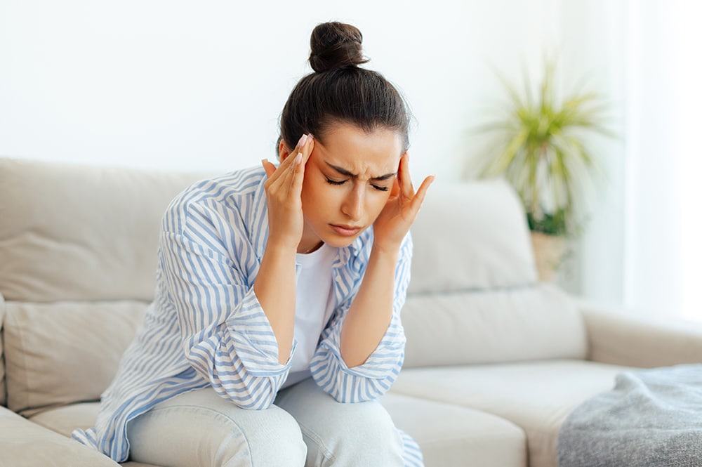 Stress, headache, illness. Upset mixed race woman sitting on a sofa in living room with eyes closed, suffering headache, vertigo, migraine, having cramp in a templess, need treatment and rest