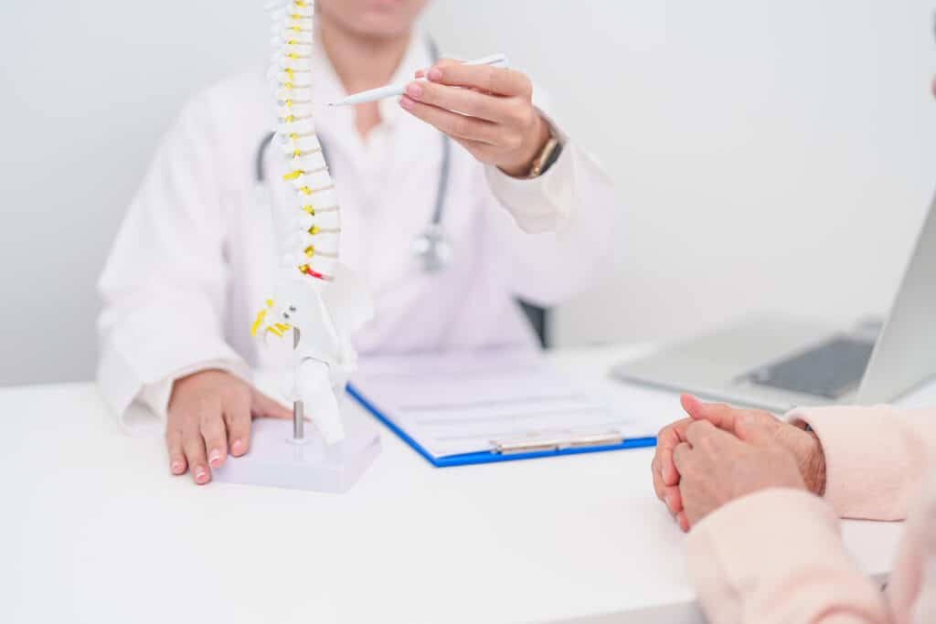 A doctor pointing to an anatomical diagram of a spine.