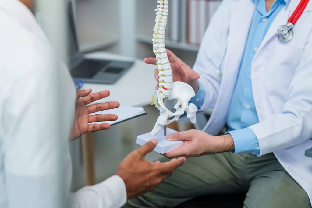 A specialist referring to a model of the human spine in a consultation with a patient