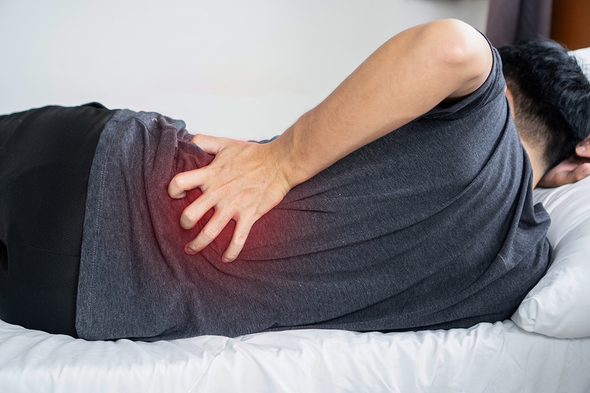 A man suffering from sciatica while lying down trying to sleep