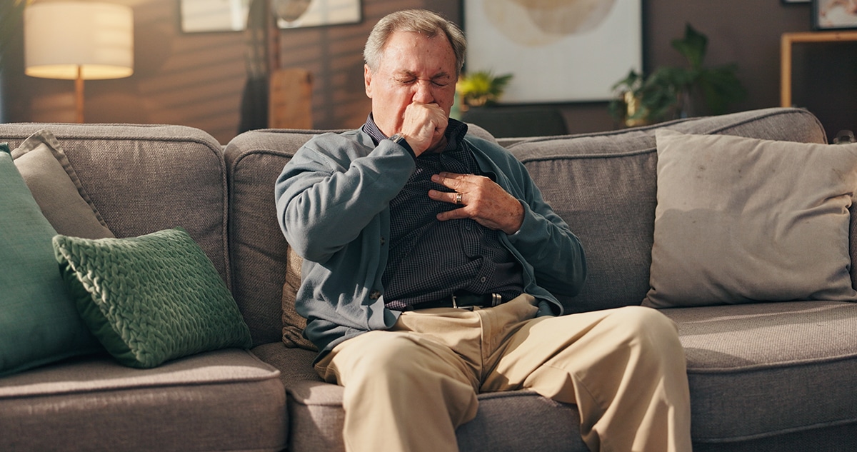 Man coughing in pain on the couch.