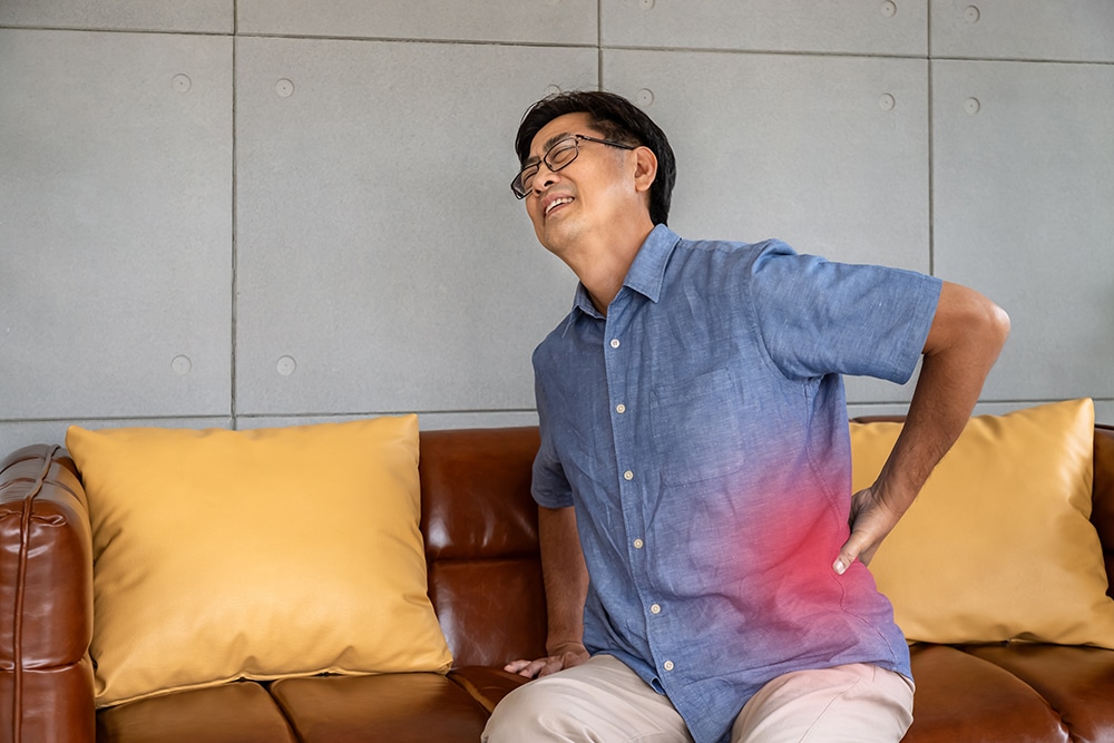 Man holding his lower back while experiencing pain caused by spinal stenosis.