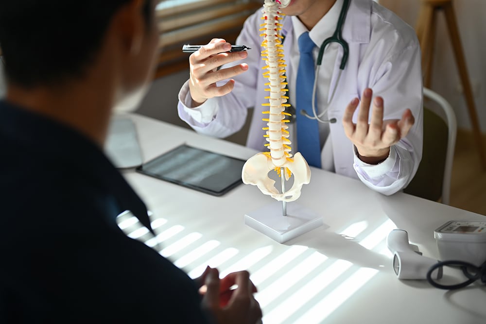 Spine specialist with a human spine anatomy model during a patient consultation.