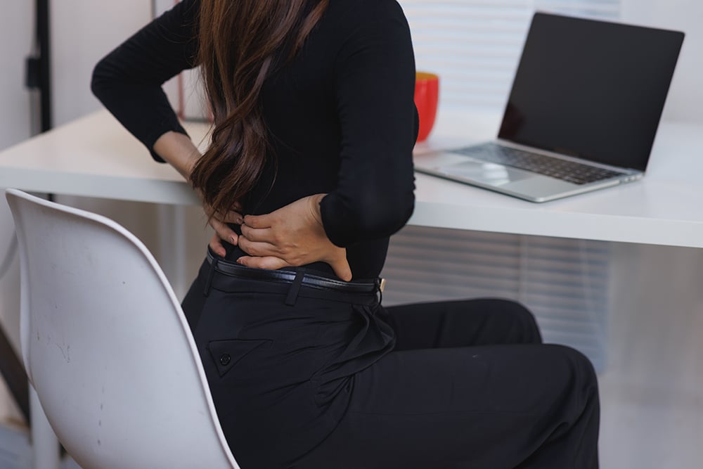 Woman seated and experiencing lower back discomfort caused by a spine condition.